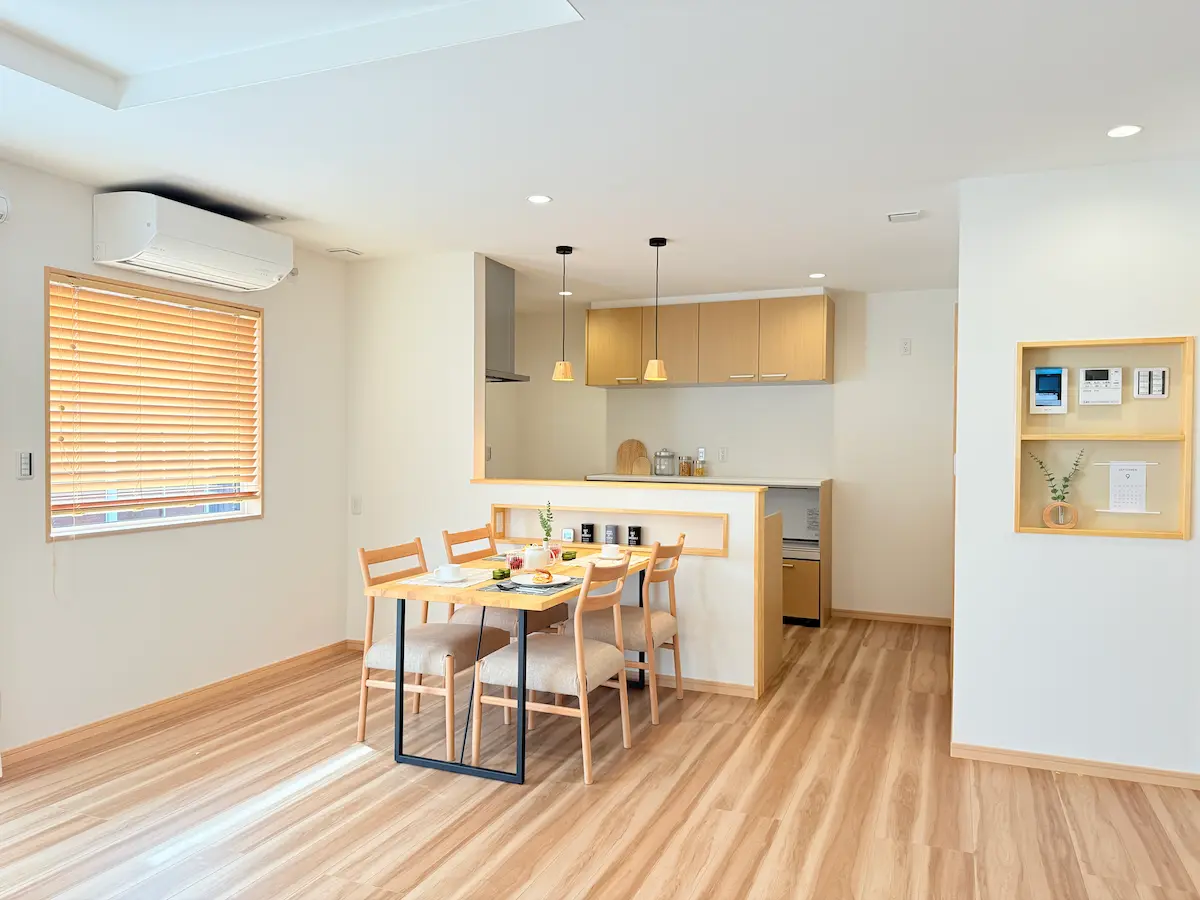 木目の造作ダイニングテーブルが置かれた明るいダイニング。食器が並ぶテーブルと、木製キッチンが調和したナチュラルな空間