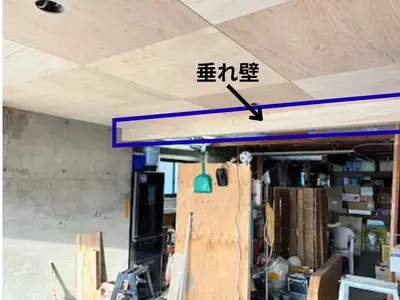 ガレージの中央に新しく設けた垂れ壁が写っており、天井の板張りと一体で空間を仕切っている様子。奥にはアウトドア用品を置く収納スペースが続いている