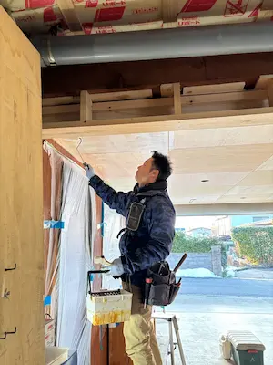 脚立に乗った作業員が、木の天井にクリア塗装をローラーで丁寧に塗っている様子。周囲には養生シートが張られ、施工中のガレージ空間が写っている